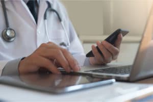 Doctor performing telemedicine or telehealth with laptop, tablet and cell phone