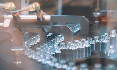 vials filled with clear liquid on a production line - idea of COVID-19 vaccine manufacturing