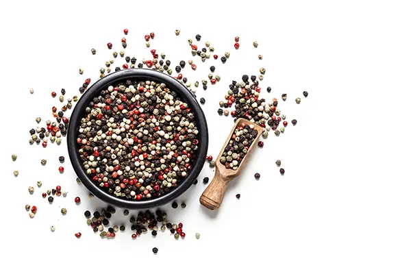 Top view of a black bowl filled with multicolored peppercorns