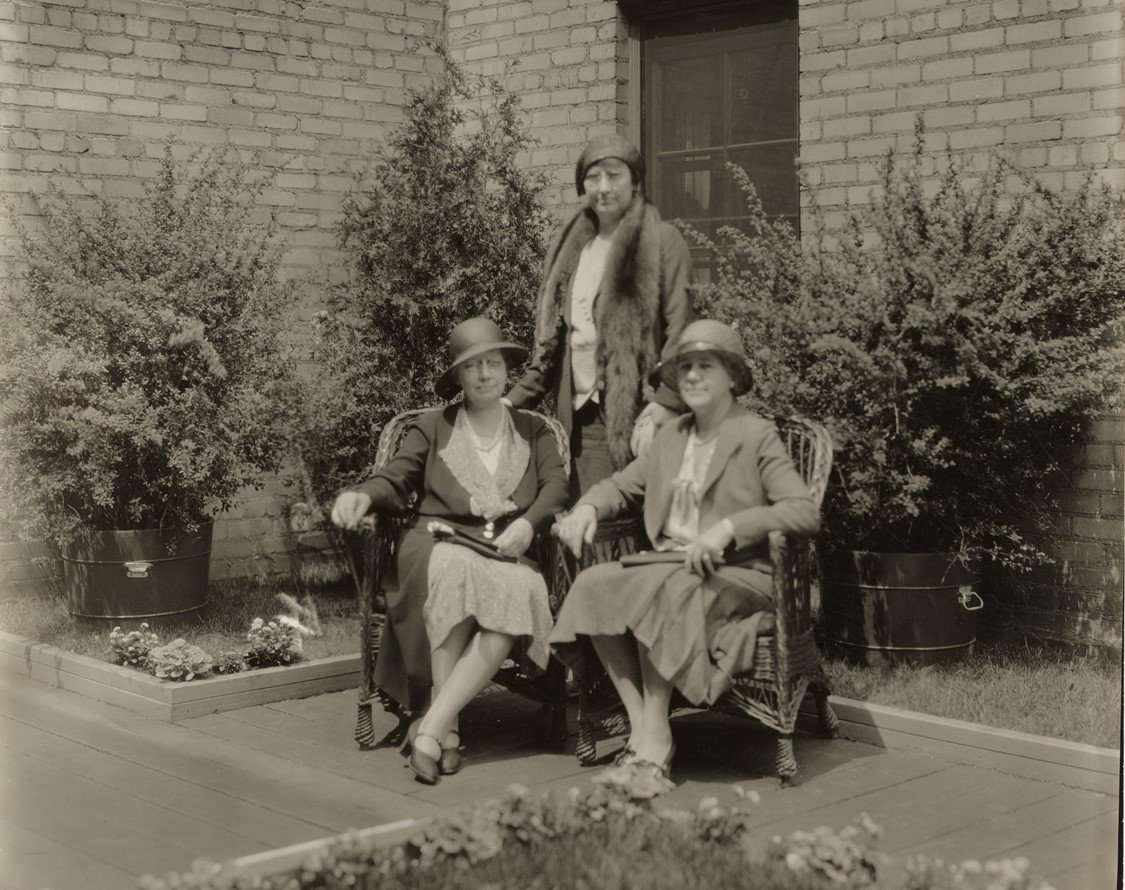 Vintage black-and-white photo of a group of women in 1920s or 1930s-era fashions sitting in a courtyard