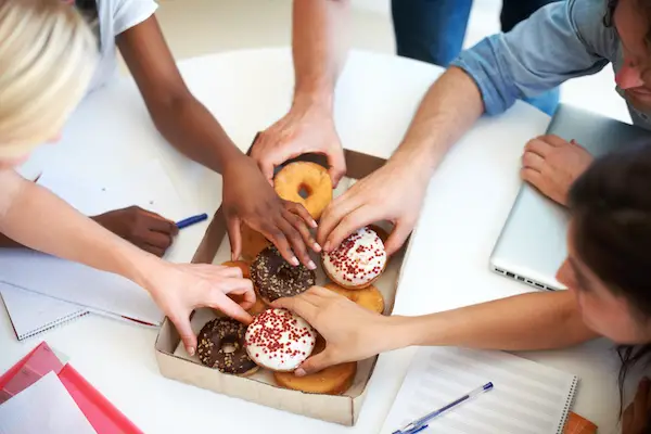Multiple people reaching inside a box of donuts